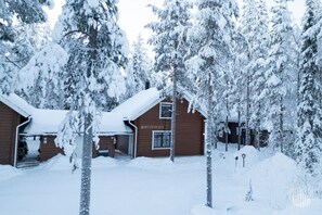 Una baita di legno con tetto imbiancato dalla neve, circondata da alberi carichi di neve.