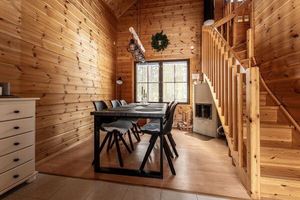 Ein Holzinnenraum mit Esstisch, Stühlen, Kamin und Treppe.