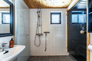 Ein Badezimmer mit einem weißen Waschbecken, einem Spiegel, einer Dusche unter einer Holzbalkendecke und einer Tür mit Fenster.