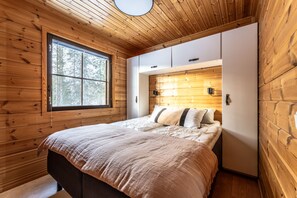 Ein Schlafzimmer mit Holzboden, einem großen Fenster, einem Bett mit weißer Bettwäsche und einem weißen Kleiderschrank.