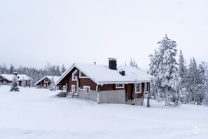 Une cabane enneigée, avec un toit en pente, entourée d’arbres chargés de neige.