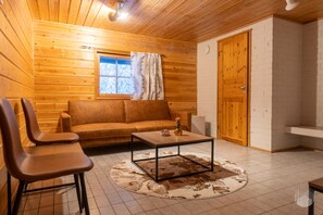 Une pièce chaleureuse avec un décor intérieur en bois, un canapé, deux fauteuils, une table basse et une fenêtre avec des rideaux.