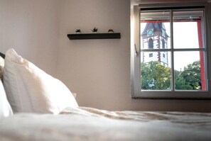 A bedroom with a bed, a window with a view of a building, and a shelf with three small plants. - Penthouse apartment—15 minutes from Europa-Park (Kenzingen)