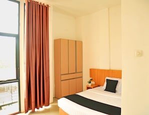 A hotel room with a bed, a wardrobe, a nightstand, and a window with curtains.