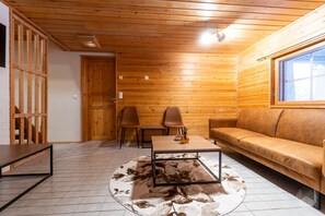 Interior de cabana de madeira com sofá, duas poltronas, mesa de centro e teto de madeira.