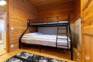 A bunk bed in a wooden cabin room with a ladder, a power outlet, and a door. - Rukakorpi 3 by Holiday in Lapland (Ruka)
