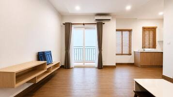 Una habitación amplia con piso de madera, una puerta corrediza que da a un balcón y una zona de kitchenette.