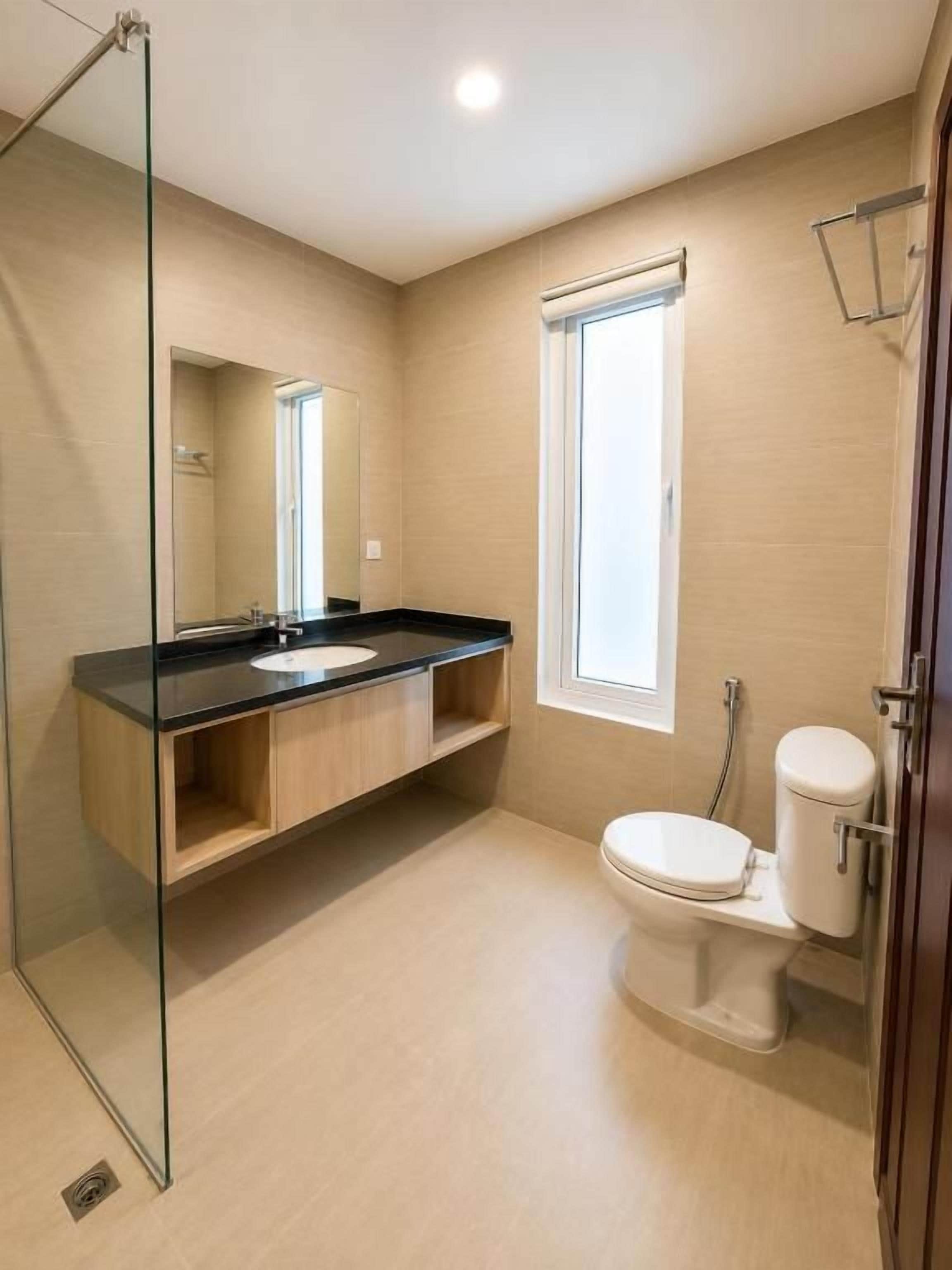 Een moderne badkamer met een glazen douchecabine, een wastafel met een zwart aanrechtblad, een toilet en een raam dat voor natuurlijk licht zorgt.