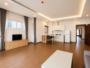 Una sala de estar moderna con un televisor de pantalla plana, una zona de comedor con sillas, una cocina con armarios y piso de madera.