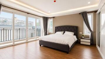 Une chambre moderne avec un grand lit, une table de chevet, une fenêtre avec des rideaux et une vue sur un bâtiment à l’extérieur.