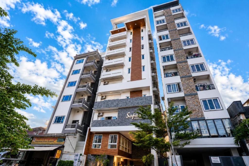 A multi-story residential building with balconies, a sign reading 'Saper Residence,' and a clear sky in the background.