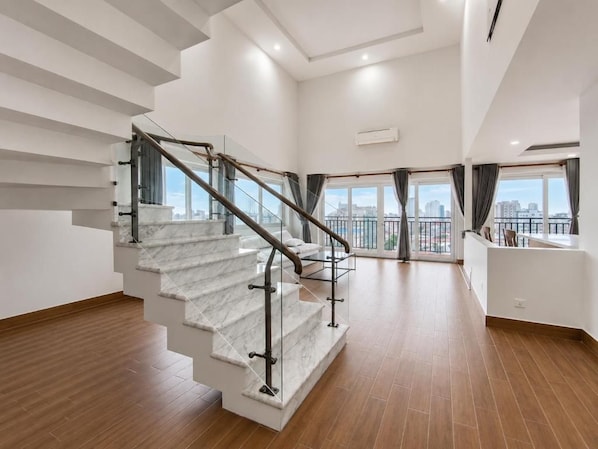 Un interior moderno con una escalera de mármol, vistas a la ciudad a través de grandes ventanales y un diseño minimalista.