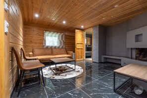 A cozy room with a wooden ceiling, a sofa, a coffee table, and a fireplace. - Rukakorpi 5 by Holiday in Lapland (Kuusamo)