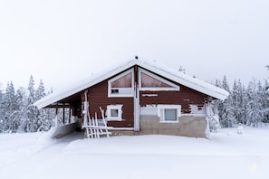 A wooden cabin with a sloped roof, surrounded by snow-covered trees. - Rukakorpi 5 by Holiday in Lapland (Kuusamo)
