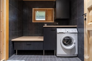 A compact laundry room with a washing machine, a bench, and a small window. - Rukakorpi 5 by Holiday in Lapland (Kuusamo)