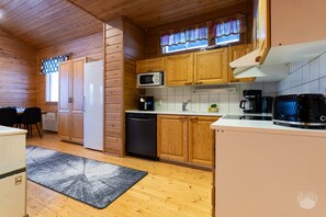 A compact kitchen with wooden cabinets, a microwave, a coffee maker, and a dishwasher. - Rukakorpi 4 by Holiday in Lapland (Ruka)