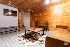 A modern living room with a wooden ceiling, a flat-screen TV mounted on a white brick wall, a sofa, two chairs, a coffee table, and a patterned rug. - Rukakorpi 4 by Holiday in Lapland (Ruka)