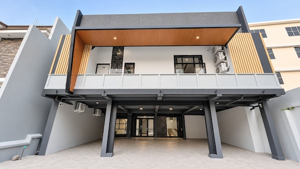 Un edificio moderno con techo plano, un área de entrada cubierta y una escalera visible que conduce al piso superior.