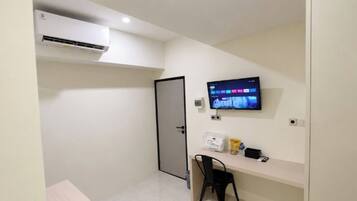 A hotel room with a flat-screen TV mounted on the wall, a desk with a chair, and a door.
