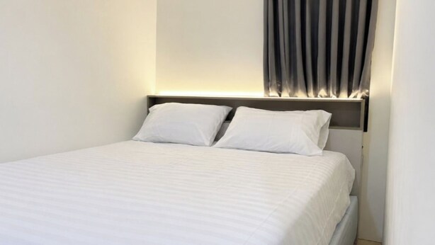 Een netjes opgemaakt bed met hoofdbord, wit beddengoed en een wandlamp.