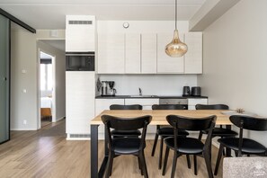 Eine moderne Küche mit einem Holztisch, schwarzen Stühlen, einem eingebauten Backofen und einer hängenden Pendelleuchte.