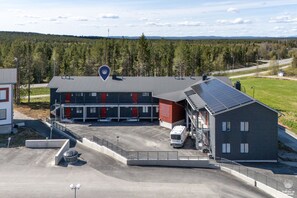 Ein Gebäude mit Parkplatz, einem Lieferwagen und einer bewaldeten Landschaft im Hintergrund.