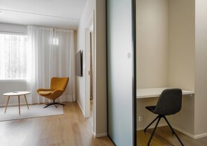 Ein modernes Zimmer mit Holzboden, einem kleinen runden Tisch, einem gelben Sessel, einem schwarzen Bürostuhl und einem weißen Schreibtisch.