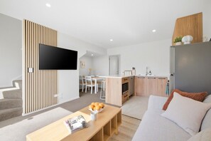 Een moderne woonkamer met een flatscreen televisie, een eethoek en een keuken met houten kastjes.