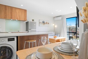 A modern kitchen with wooden cabinets, a washing machine, and a dining area with a table set for two. - Stylish 3BR Ensuite, CBD, Car Park, Stadium Nearby (Christchurch)
