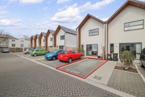 A parking area with multiple cars, a manhole cover, and a building with a modern design. - Stylish 3BR Ensuite, CBD, Car Park, Stadium Nearby (Christchurch)