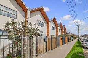 Een rij moderne huizen met schuine daken en houten details, een hekpoort en een groene gazon.