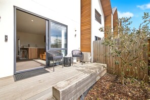 Een modern huis met een schuifdeur naar een keuken, een terras met tuinmeubilair en een houten omheining.