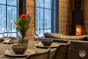 A cozy dining area with a fireplace, wooden walls, and a view of a snowy forest. - Villa SnowLife B by Holiday in Lapland (Levi)