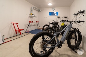 A room with a bike rack holding two mountain bikes, a red chair, a blue mat, and a clock on the wall. - Villa SnowLife B by Holiday in Lapland (Levi)