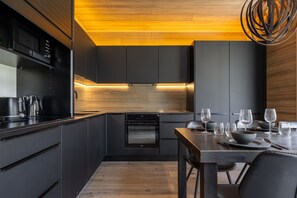 A modern kitchen with dark cabinetry, a built-in oven, and a dining area with a wooden table and chairs. - Villa SnowLife B by Holiday in Lapland (Levi)