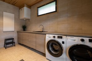 A compact kitchen with a built-in washing machine, a sink, and a small stool. - Villa SnowLife B by Holiday in Lapland (Levi)