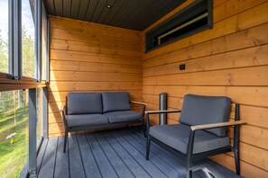 En stuga av trä med en balkong som har två stolar och en soffa.