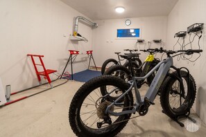 A room with a bike rack holding two mountain bikes, a red chair, a blue mat, and a clock on the wall. - Villa SnowLife A by Holiday in Lapland (Levi)