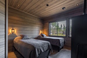 A cabin with two beds, wooden walls, and a large window with a view of trees. - Villa SnowLife A by Holiday in Lapland (Levi)