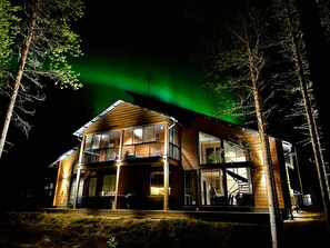 A two-story wooden house with large windows and a balcony, surrounded by trees. - Villa SnowLife A by Holiday in Lapland (Levi)