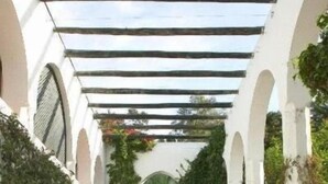 Een buiten eethoek met tafels en stoelen, overdekt door een pergola, omringd door bogen en groen.