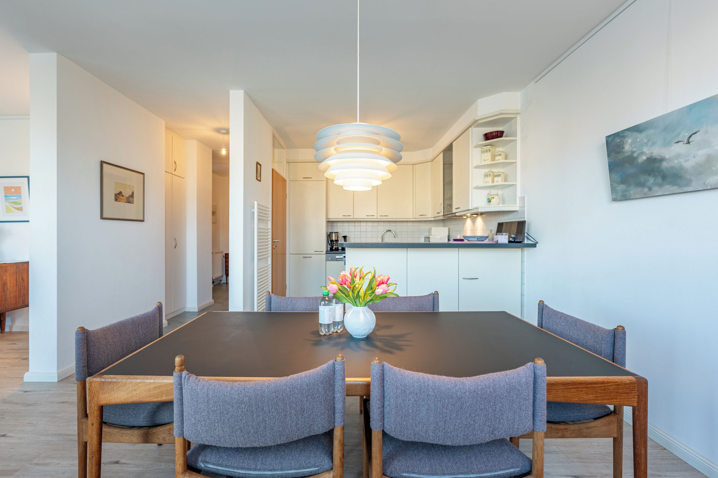 Ein moderner Essbereich mit einem dunklen Holztisch, grau gepolsterten Stühlen und einer Blumenvase.