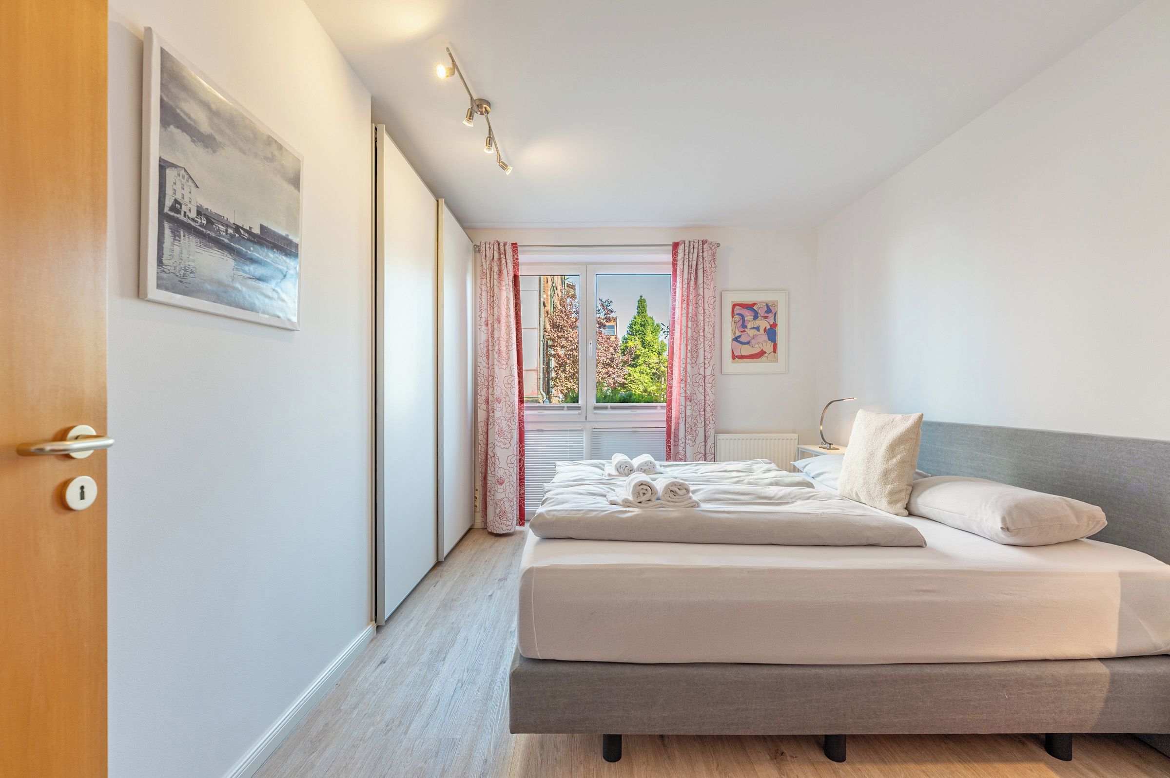 Ein modernes Schlafzimmer mit Bett, Tür, Fenster mit Vorhängen und einem Bild an der Wand.