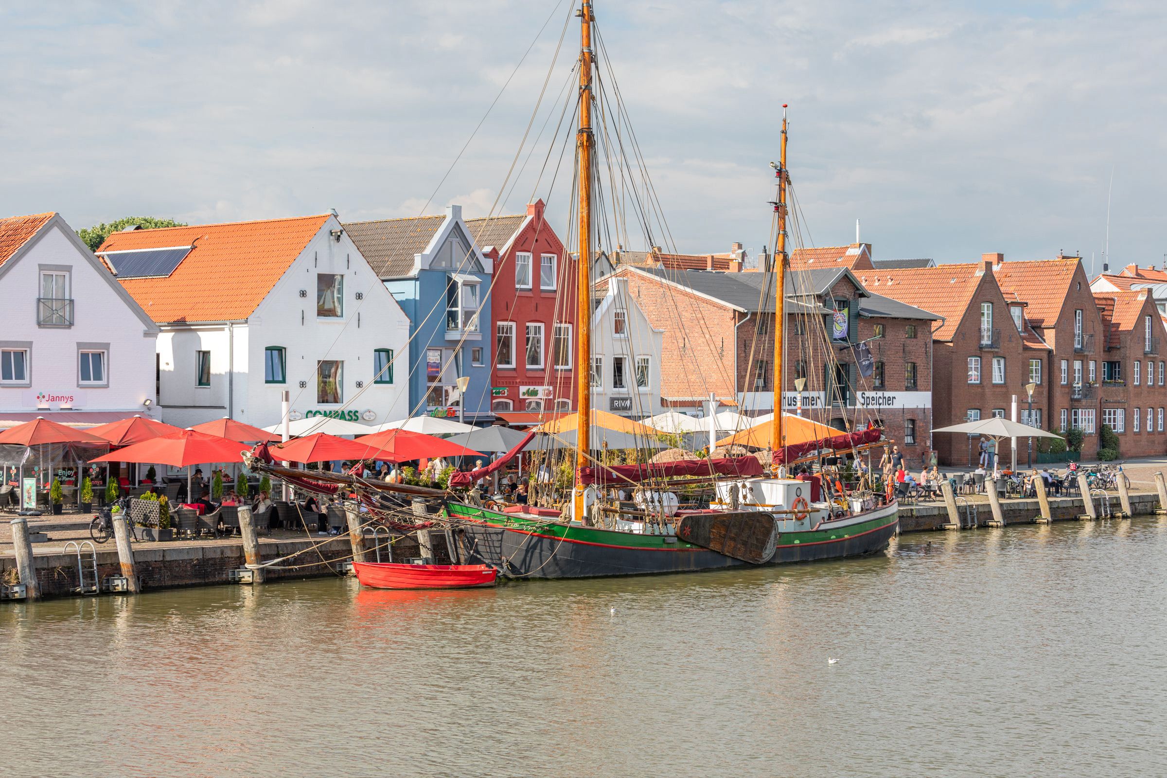 A waterfront with traditional buildings and a sailing ship docked.