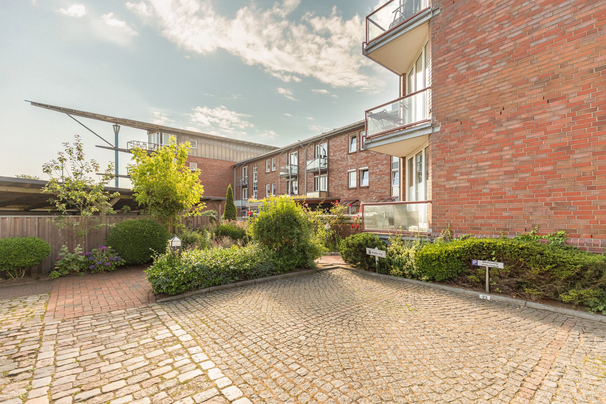 Een binnentuin met een bakstenen gebouw, een verhard pad en diverse beplanting.