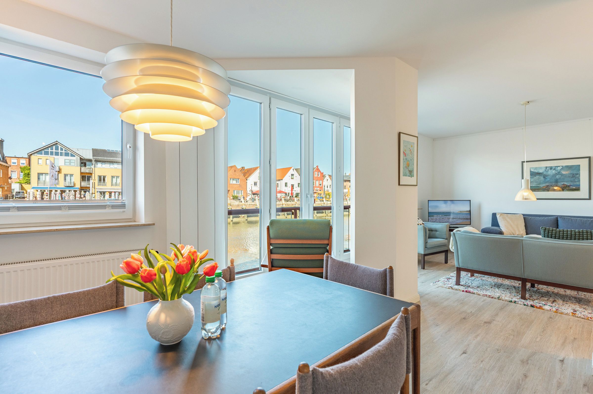 A modern living room with a dining area, large windows, and a view of buildings outside.