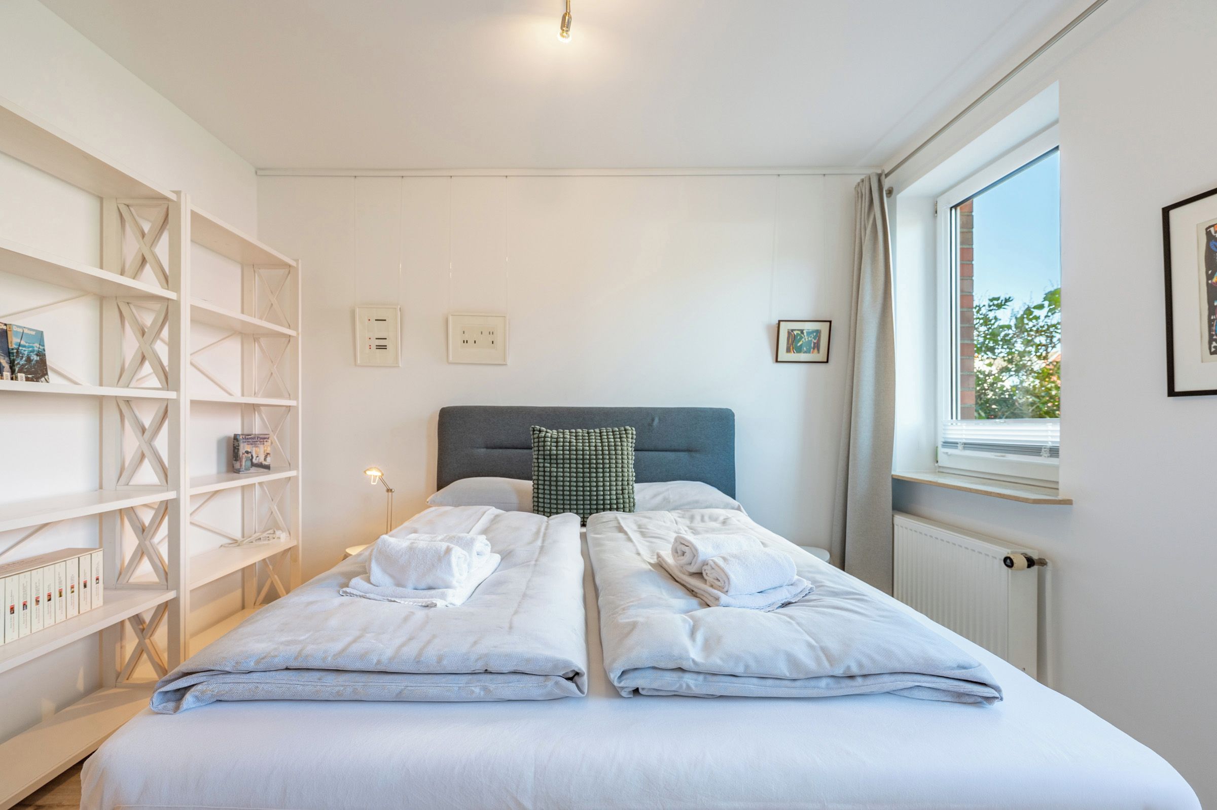 A bedroom with two beds, a bookshelf, a radiator, and a window.
