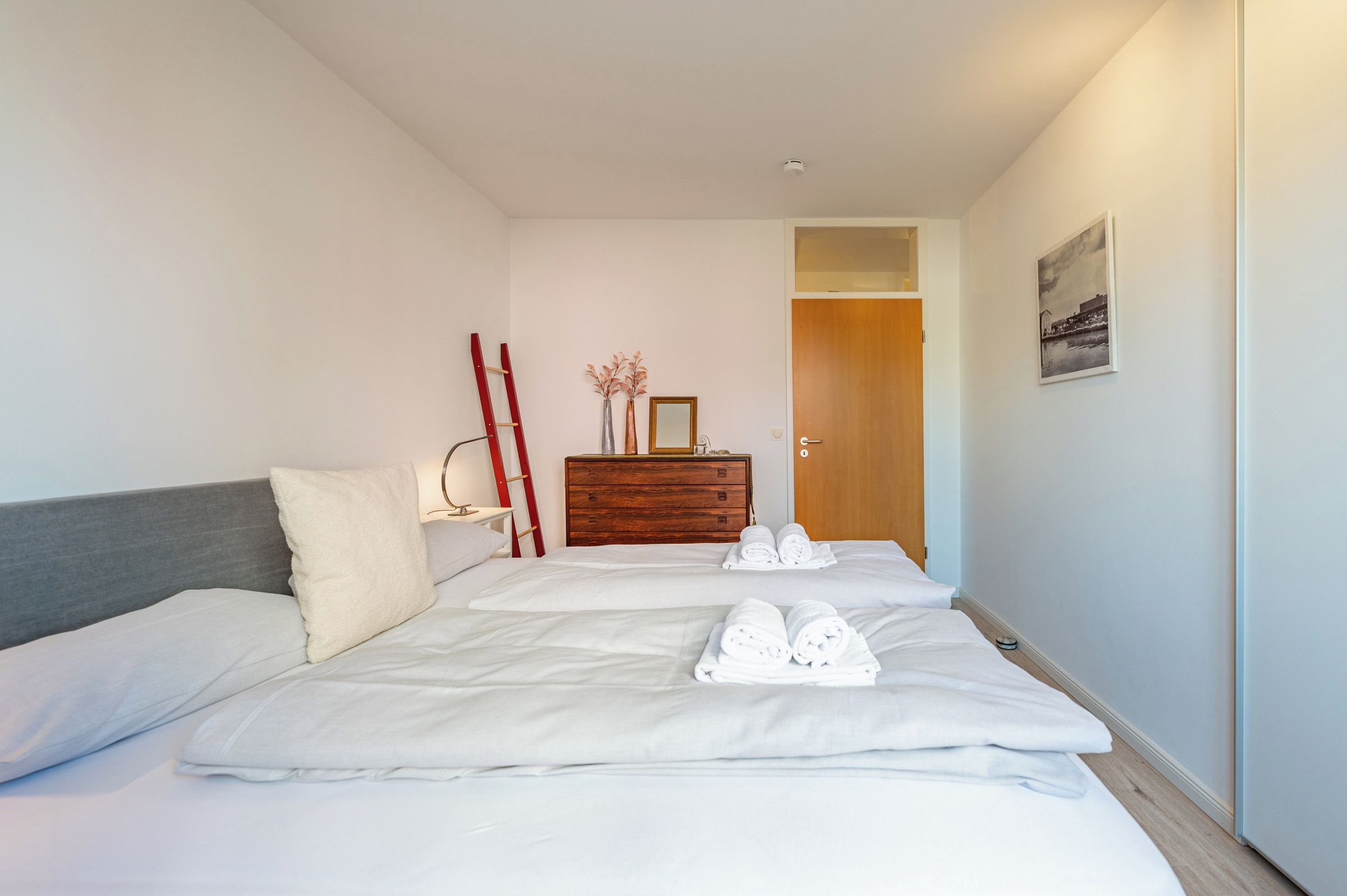 Ein Hotelzimmer mit einem Bett, einem Nachttisch, einer Kommode und einer Tür zu einem anderen Raum.