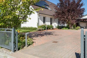 Ein Wohnhaus mit gepflasterter Auffahrt, einem weißen Gebäude und einem Garten mit verschiedenen Pflanzen und Blumen.