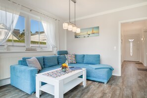 Una sala moderna con un sofá azul, una mesa de centro blanca y un cuadro de veleros en la pared.